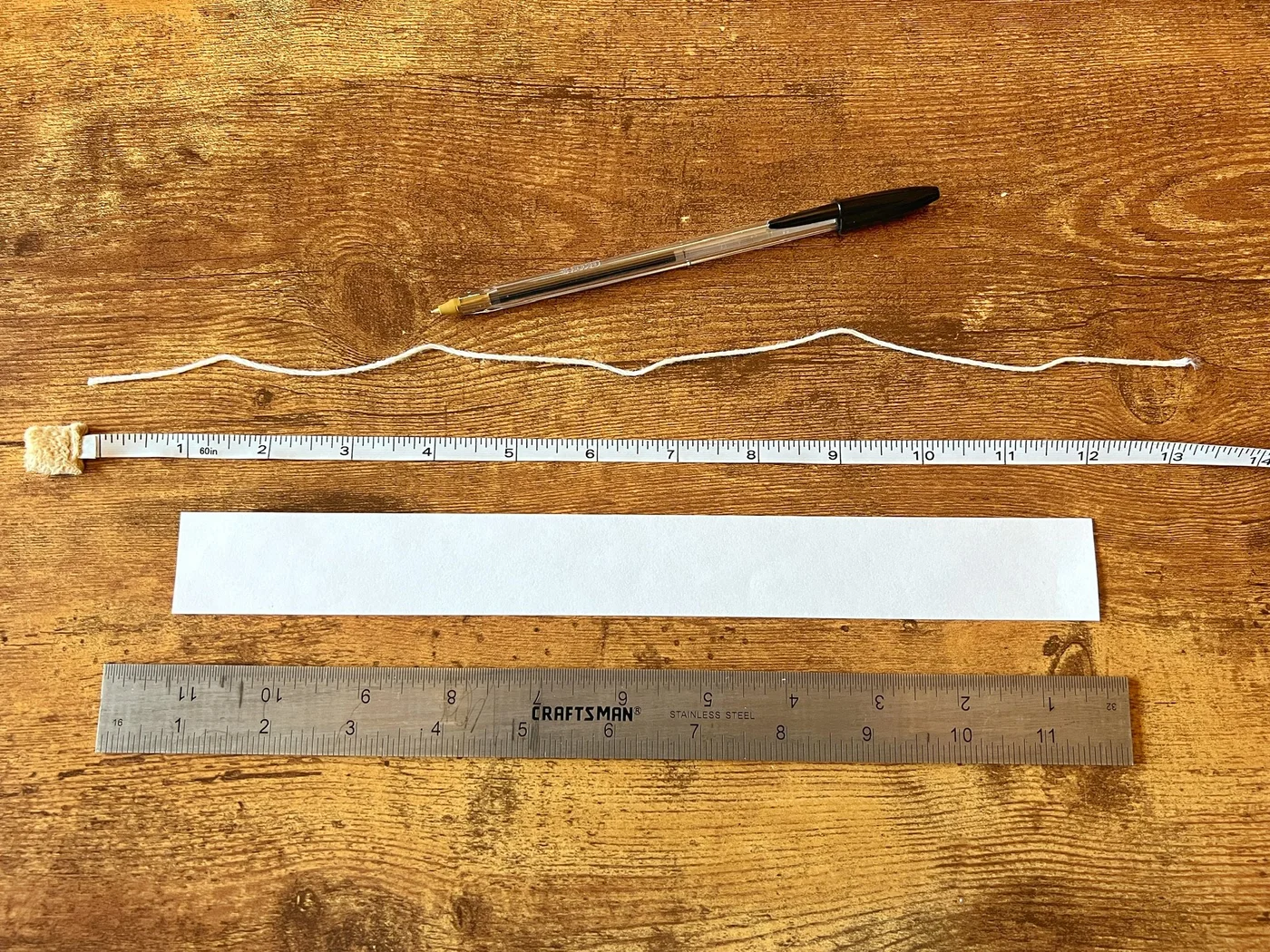 A ruler, measuring tape, string, pen, and paper for measuring a wrist